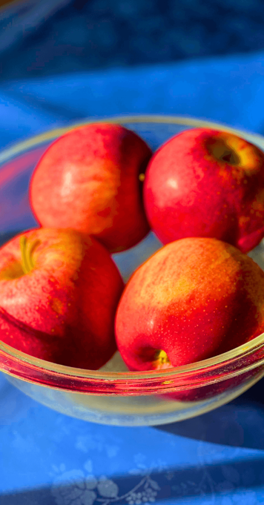 four red gala apples in a glass bowl on a table