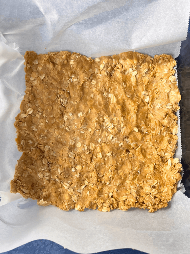 peanut butter and oat mixture pressed into parchment lined square pan