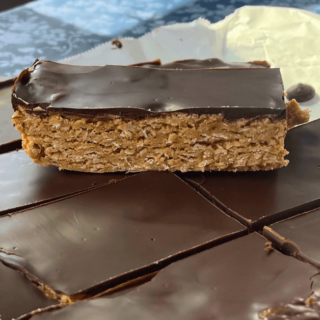 up close shot of a cut peanut butter and dark chocolate oat bar on parchment paper with one on top of the others exposing the layers