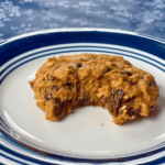 a oatmeal pumpkin chocolate chip cookie with a bite taken out of it sitting on a small blue and white plate
