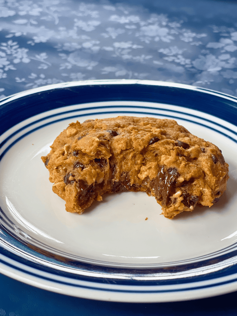 a oatmeal pumpkin chocolate chip cookie with a bite taken out of it sitting on a small blue and white plate