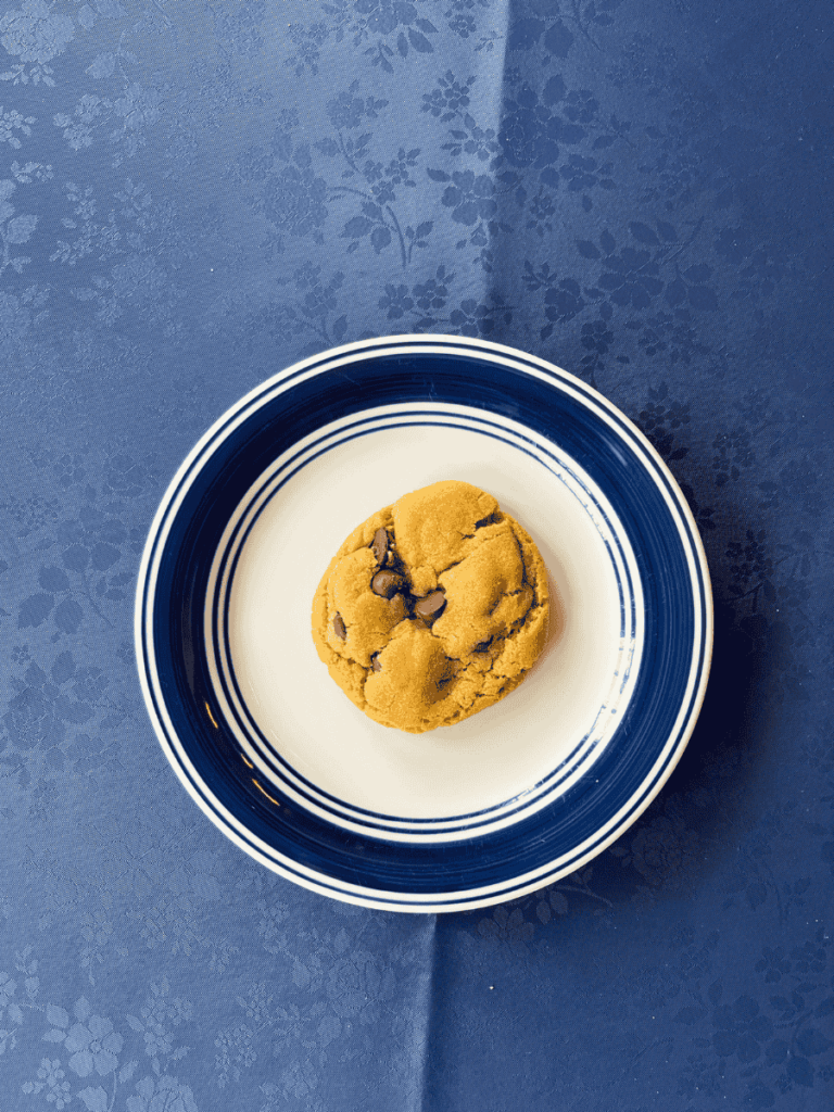 overheard shot of soft peanut butter chocolate chip cookie on a plate set on a table with a blue table cloth