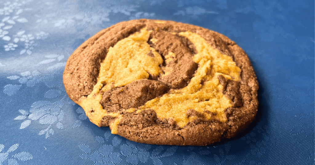 side shot of peanut butter brownie swirl cookie sitting on a blue floral table cloth