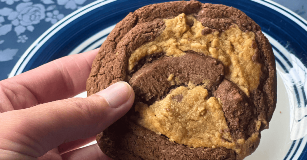 hand holding a peanut butter brownie swirl cookie above a small white and blue plate
