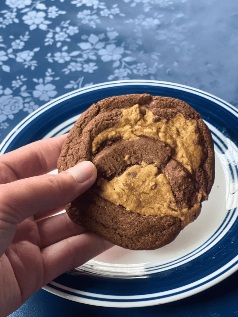 hand holding a peanut butter brownie swirl cookie above a small white and blue plate