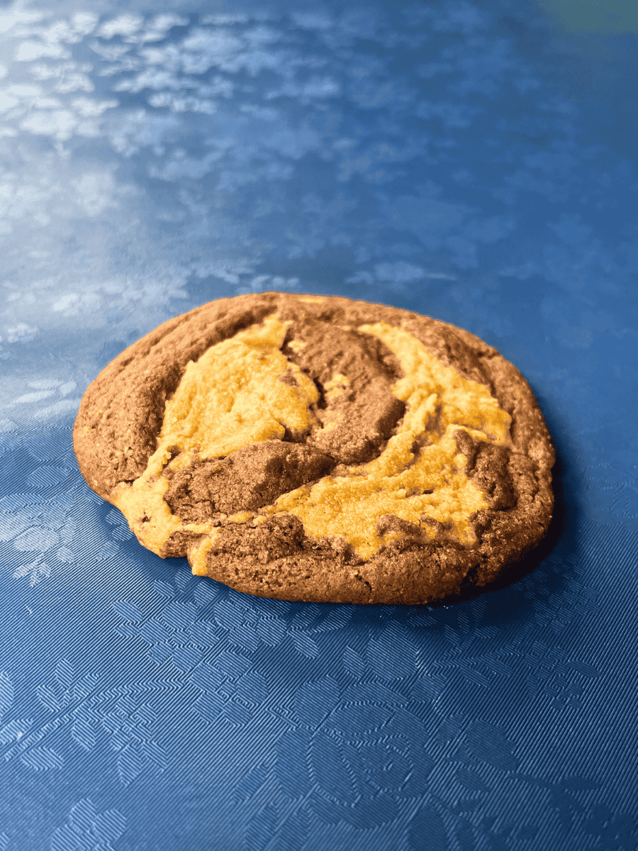 side shot of peanut butter brownie swirl cookie sitting on a blue floral table cloth