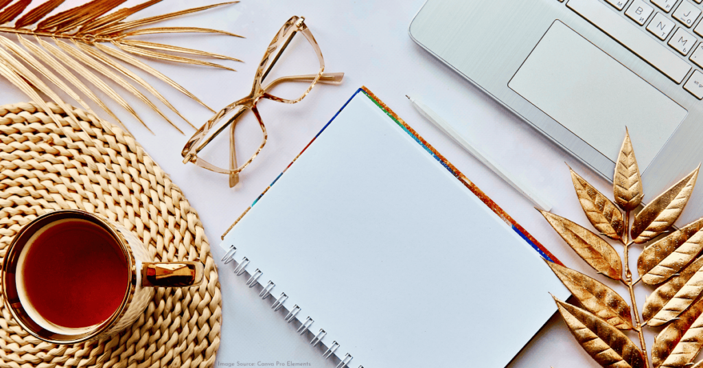natural aesthetic overhead shot of a desk with a gold cup of tea resting on a woven coaster, a pair of tan glasses, and a blank white notepad next to an opened laptop