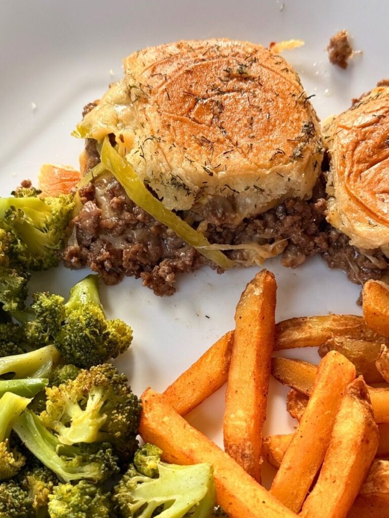 close shot of mississippi sliders served on a white dinner plate with french fries and roasted broccoli