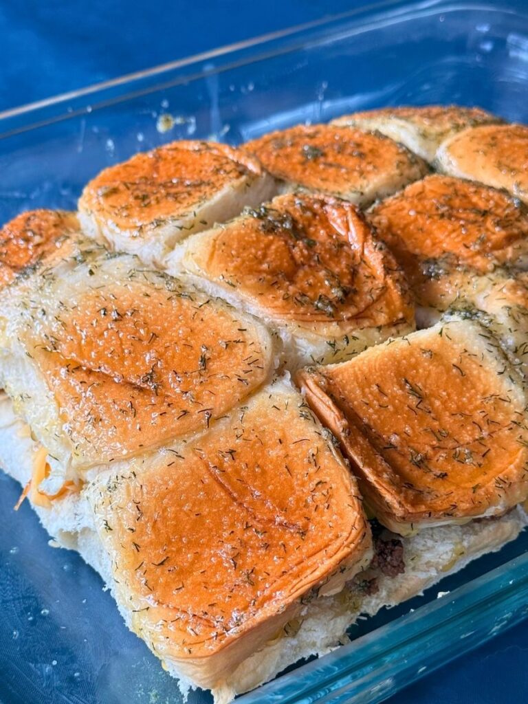 mississippi sliders prepped for oven with seasoned butter topping added to the tops of the rolls in a 13" x 9" glass pan