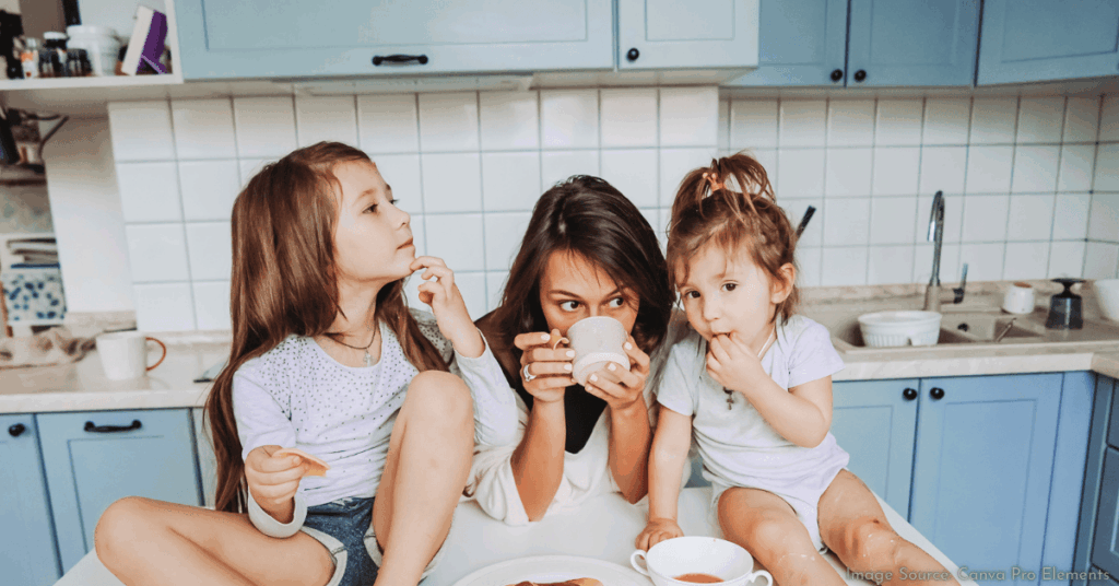 mom sipping coffee in the kitchen with a daughter sitting on each side of her