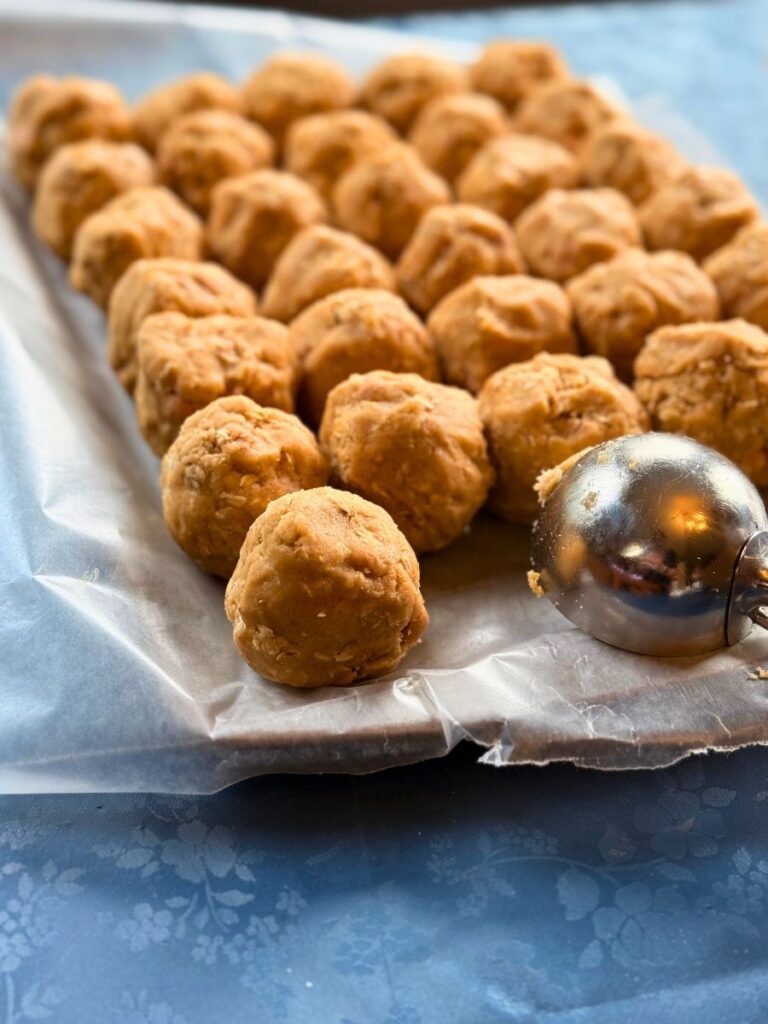 peanut butter oatmeal cookie dough balls resting on wax paper with a large cookie scoop resting next to them