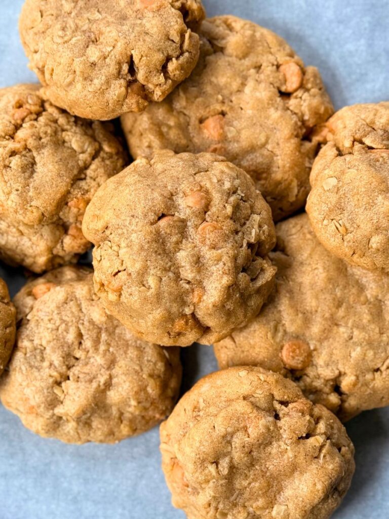 a pile of peanut butter oatmeal cookies with butterscotch chips resting on parchment paper