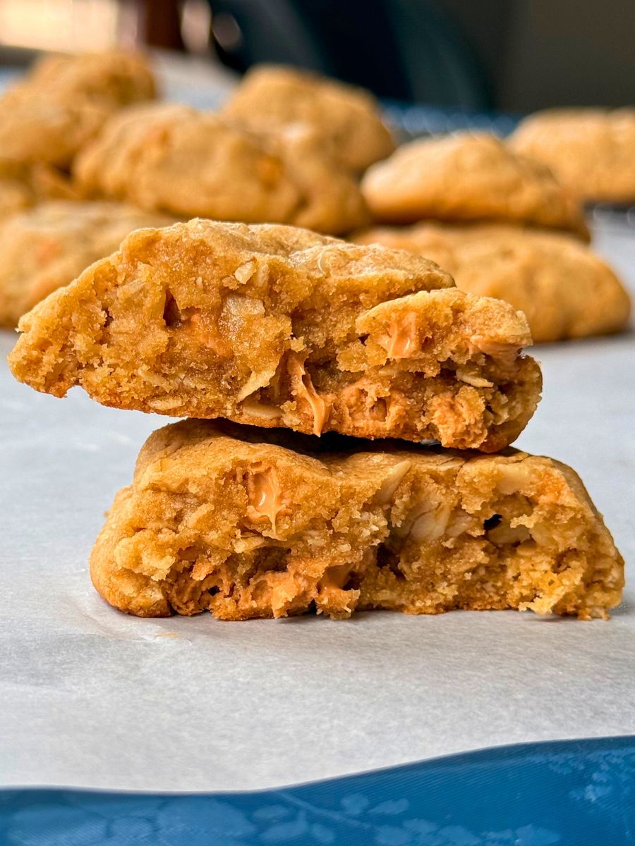 a peanut butter oatmeal cookie with butterscotch chips broke in half with one half stacked on the other exposing the inside of the cookie