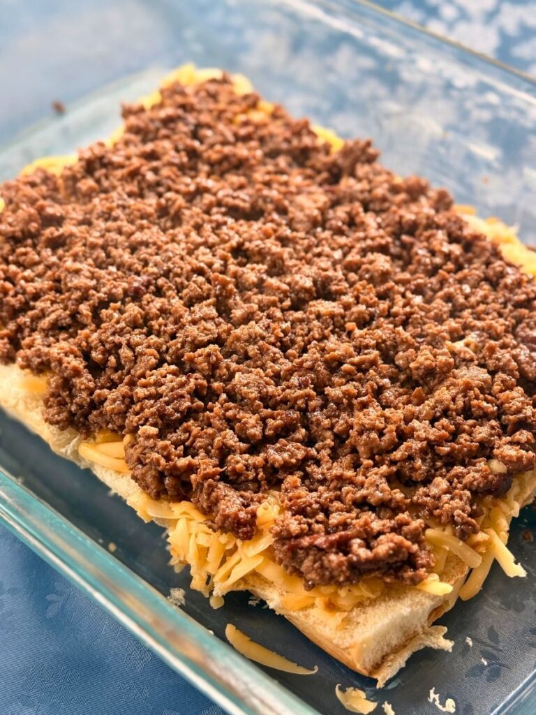 slider rolls topped with shredded gouda and mississippi seasoned ground beef in a glass 13" x 9" pan