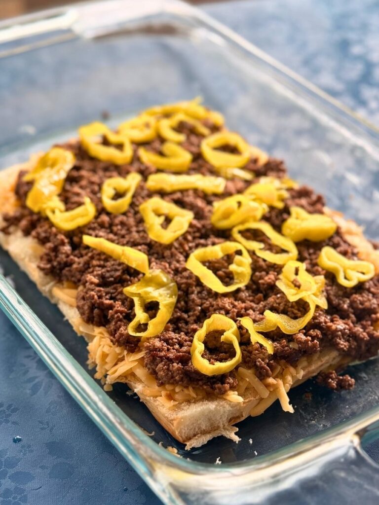 slider rolls topped with shredded gouda and mississippi seasoned ground beef and pepperoncinis in a glass 13" x 9" pan