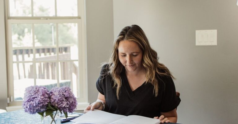 mom sitting at table that has a glass jar of purple hydrangeas on it looking at her planner