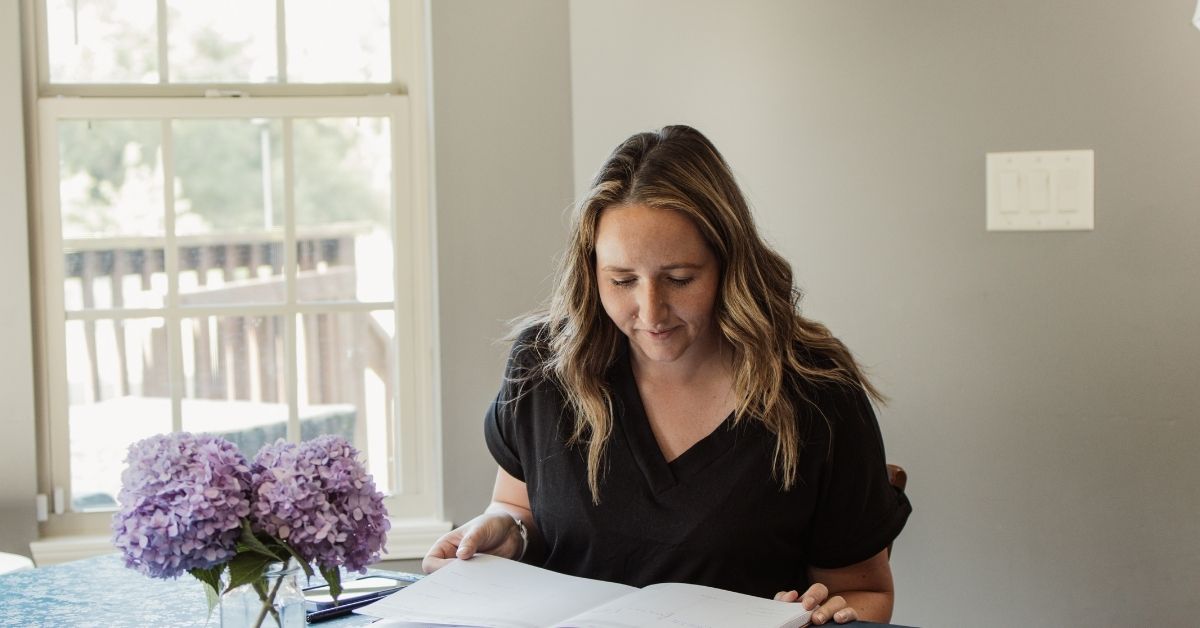 mom sitting at table that has a glass jar of purple hydrangeas on it looking at her planner