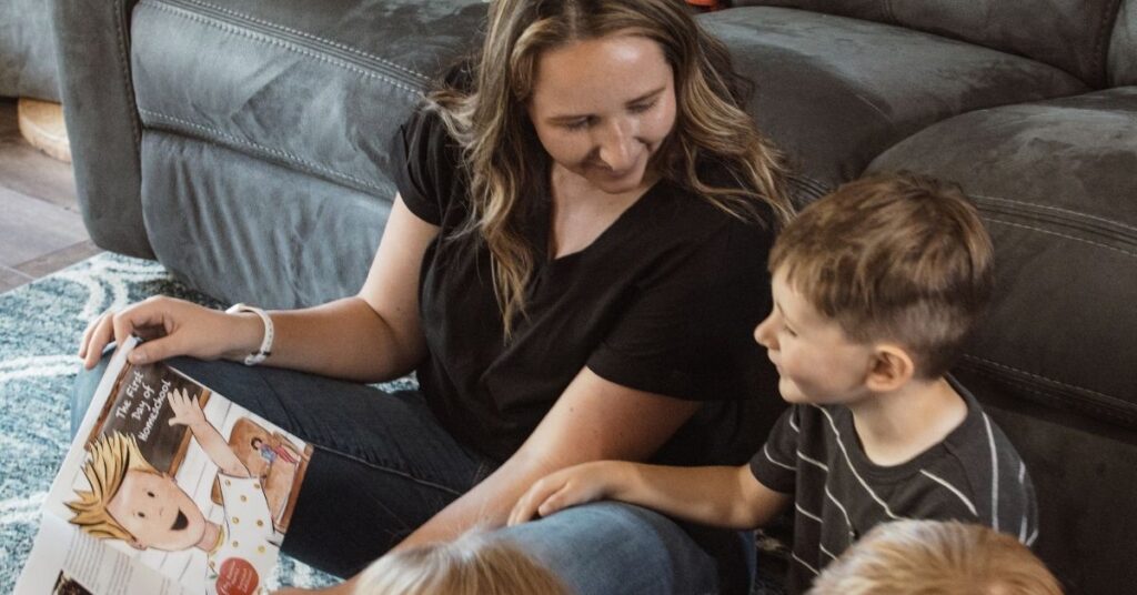 mom sitting on the floor in front of the couch reading to three toddlers