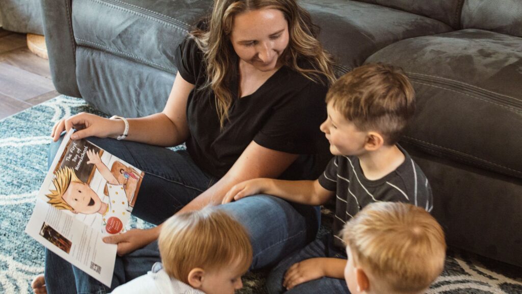 mom sitting on the floor reading a book to her three toddlers